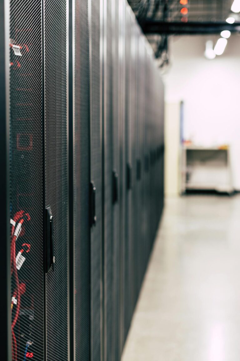Metal black cabinets with servers inside with red wires connected standing in row in lighted room